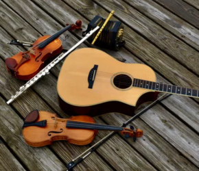 Photograph of an acoustic guitar, an squeezebox, a violin, a fiddle, and two kinds of flute laid against a wood plank background