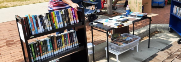 Photograph of the lirabry's book sale, with a black book cart full of books and a folding table with various handouts
